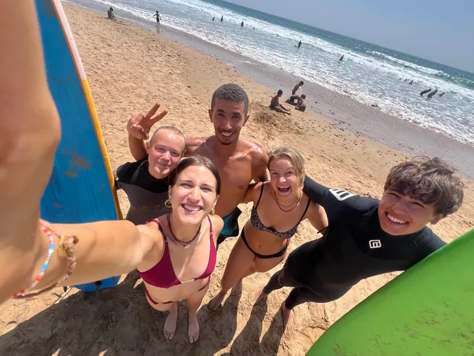Group of four young surfers smiling with coach Simo after a group surf session on the Agadir coast
